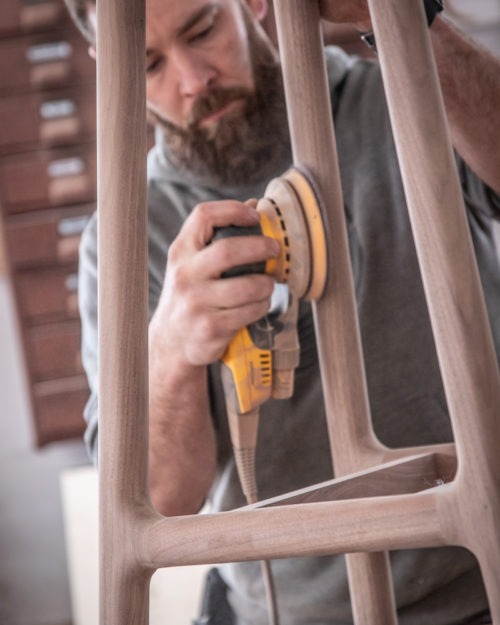 A Seven Trees Woodworking employee sanding the sides of a wooden stool