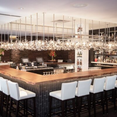 White-backed bar stools next to a bar with a wooden countertop and brick sides remodeled by commercial millworkers from Seven Trees Woodworking