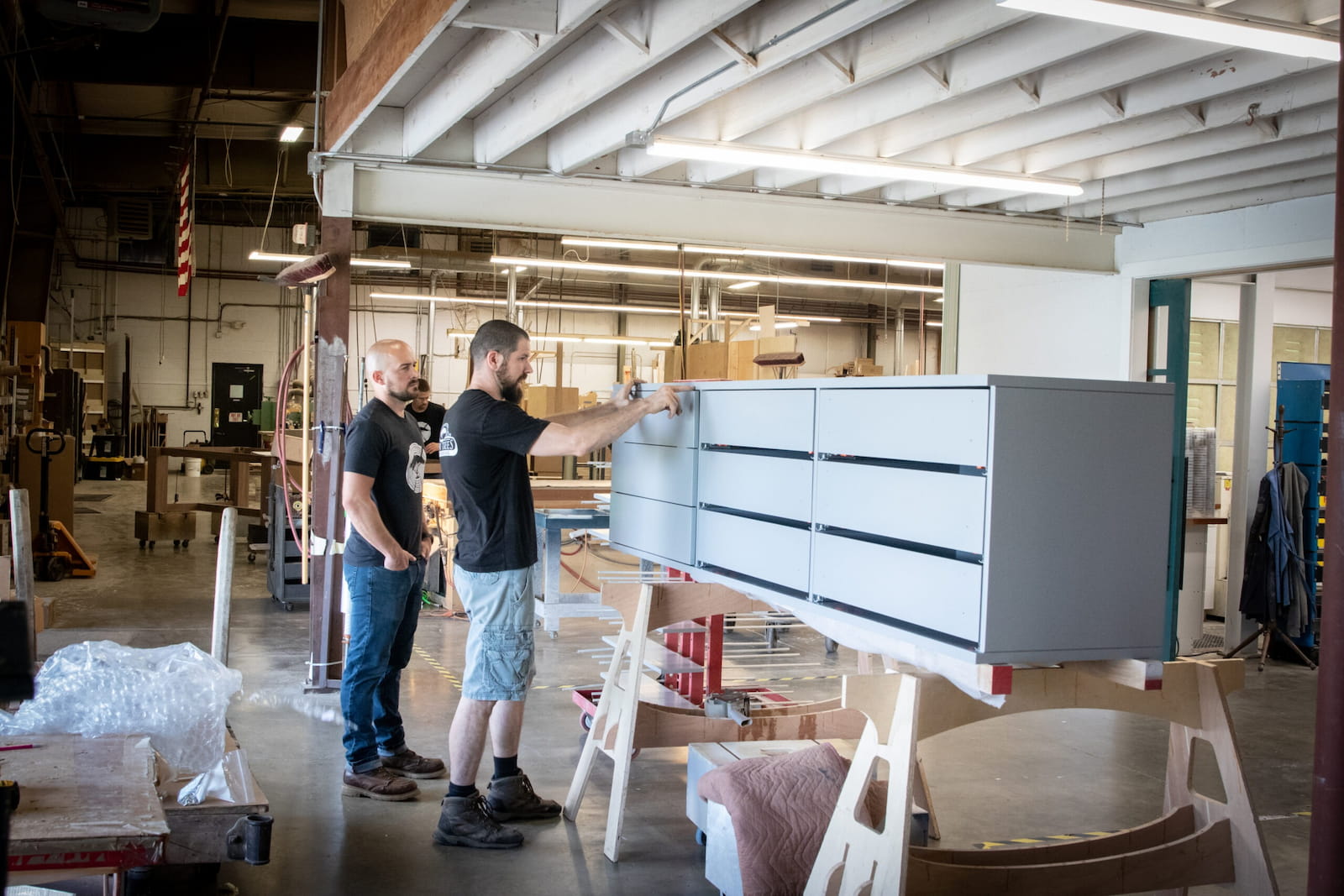 Two Seven Trees Woodworking employees putting finishing touches on a grey cabinet